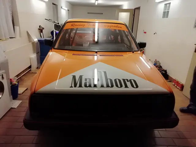 VW Golf Rallyeauto in Orange und Weiß mit Frontfolierung in der Garage